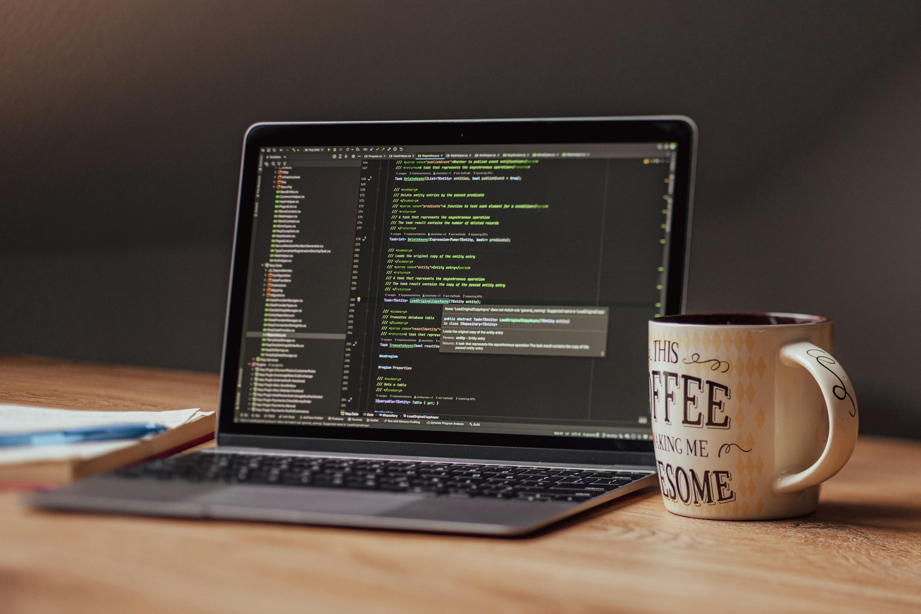 A laptop showing code next to a coffee mug